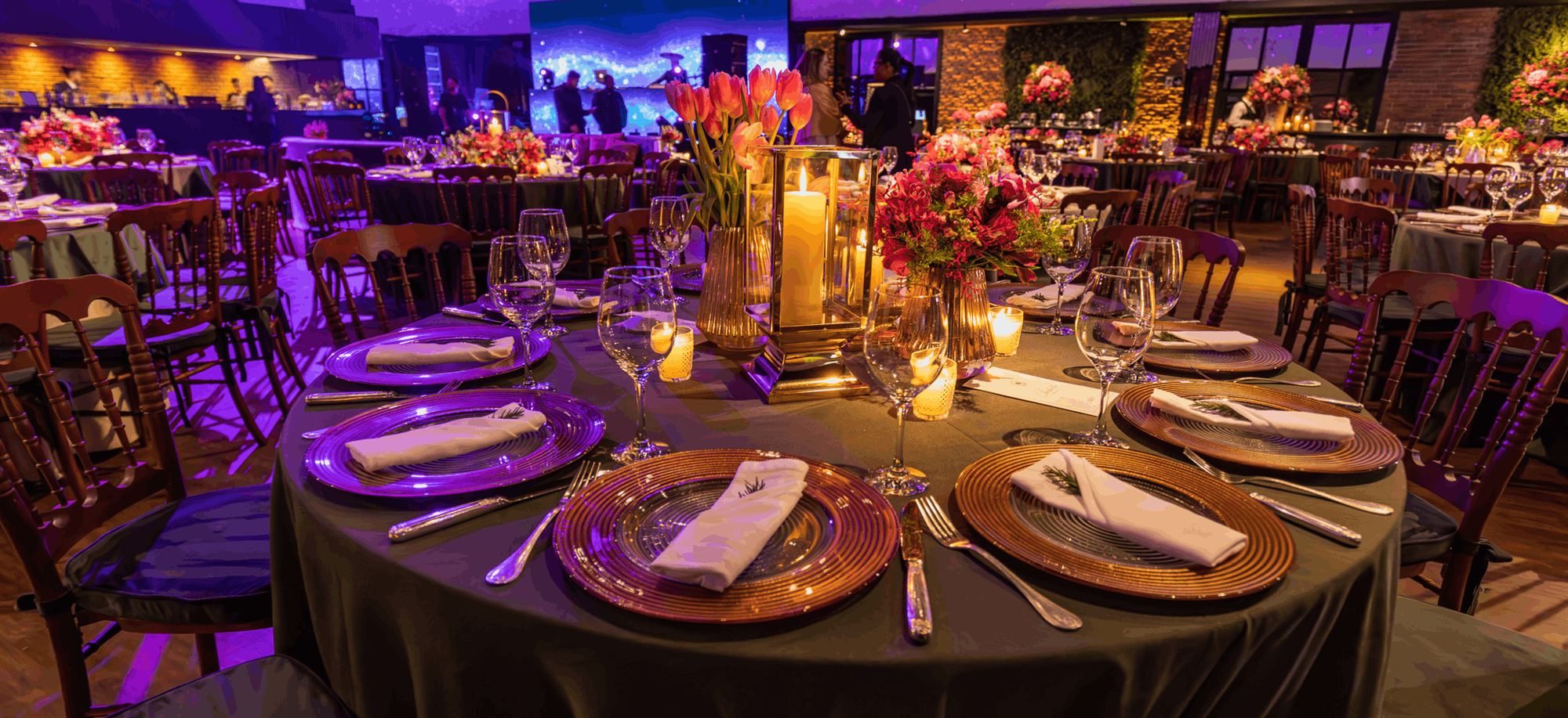 Candlelit gala dinner tables set with flowers and glassware in a busy event venue