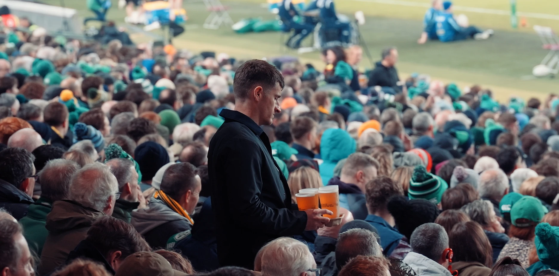 Staff member delivering pints to fans in their seats at a packed Aviva Stadium rugby match